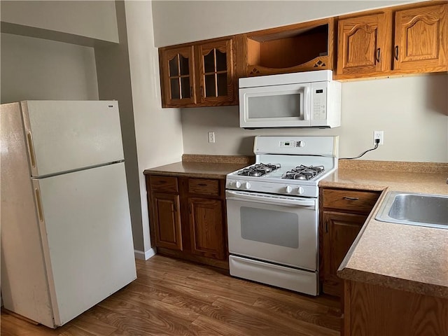 kitchen featuring white appliances, glass insert cabinets, brown cabinetry, dark wood-style flooring, and a sink