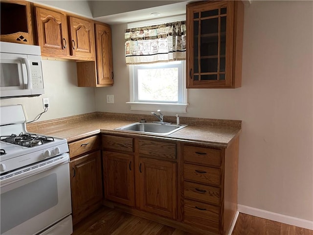 kitchen featuring white appliances, glass insert cabinets, dark wood-type flooring, brown cabinets, and a sink