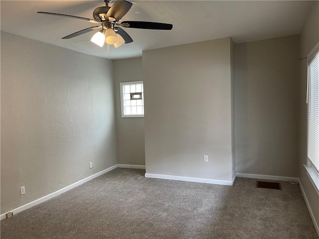 carpeted empty room with ceiling fan, baseboards, visible vents, and a wealth of natural light