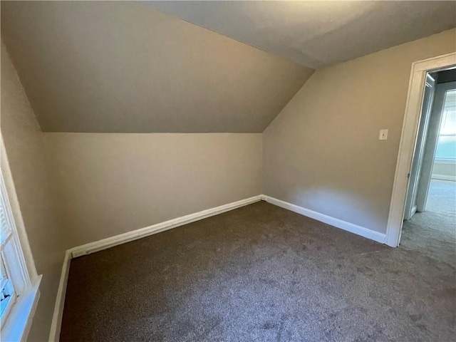 additional living space with baseboards, dark colored carpet, and lofted ceiling