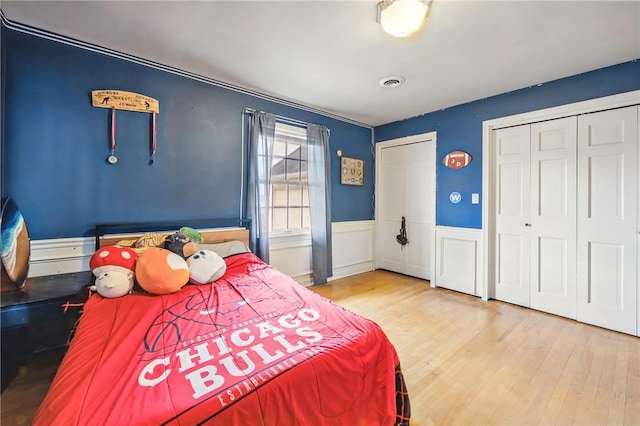 bedroom featuring visible vents, wainscoting, two closets, and wood finished floors