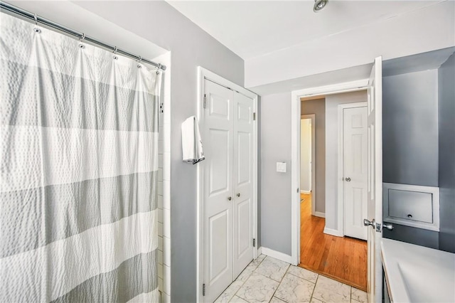 full bath with a shower with shower curtain, marble finish floor, and baseboards