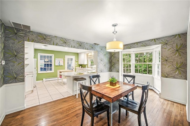dining space with light wood-type flooring, visible vents, a baseboard radiator, wallpapered walls, and baseboards