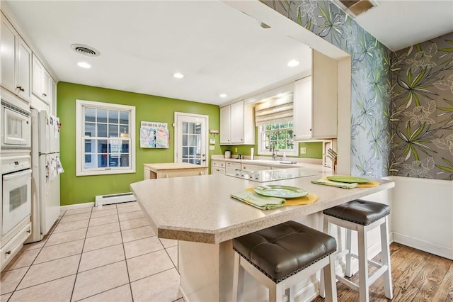 kitchen with white appliances, visible vents, baseboard heating, light countertops, and wallpapered walls