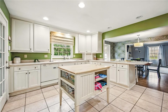 kitchen featuring dishwasher, a sink, a peninsula, white cabinetry, and wallpapered walls