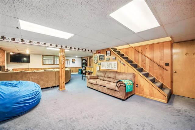 living area featuring wood walls, stairway, and a paneled ceiling