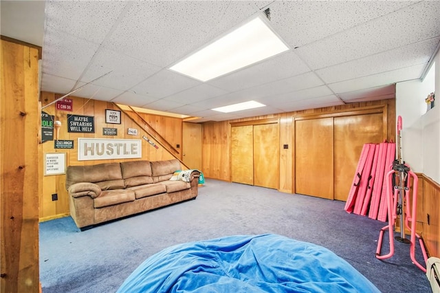 carpeted living room with baseboard heating, wooden walls, and a drop ceiling