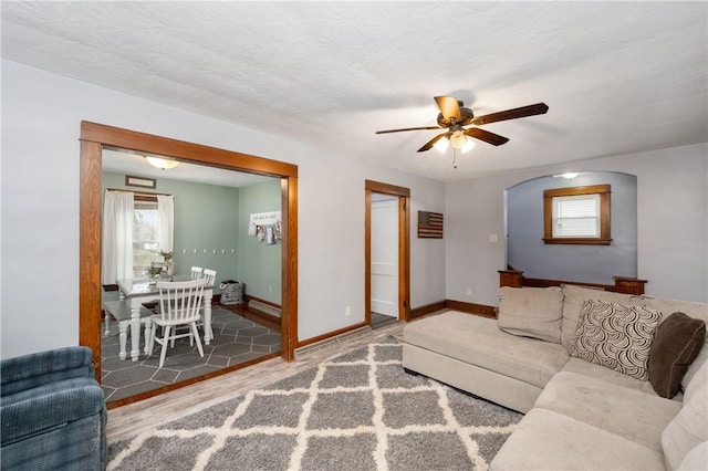 living room with arched walkways, baseboards, a ceiling fan, and wood finished floors