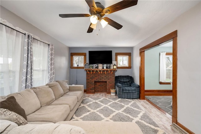 living room with baseboards, light wood-style floors, a brick fireplace, and a ceiling fan