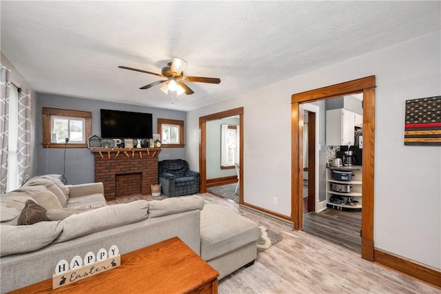 living area featuring light wood-type flooring, a brick fireplace, baseboards, and a ceiling fan