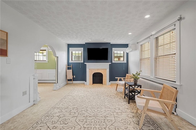 living room featuring arched walkways, a wall mounted AC, a fireplace, a textured ceiling, and light colored carpet