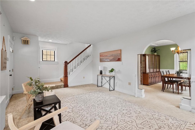 living area featuring baseboards, arched walkways, light carpet, and stairs