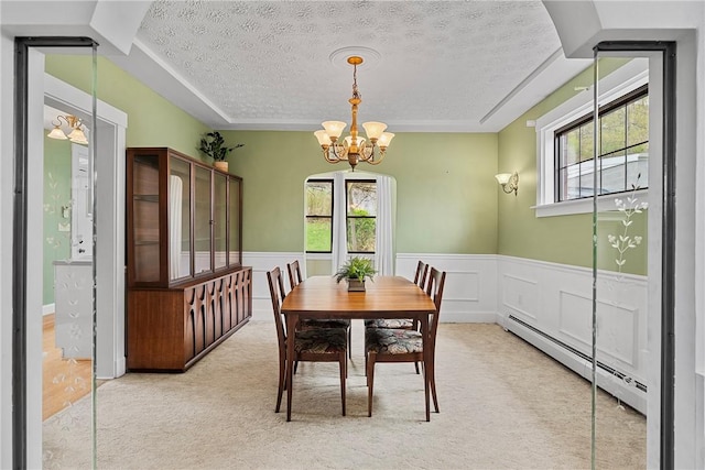 carpeted dining room with a chandelier, a textured ceiling, a baseboard heating unit, and a healthy amount of sunlight