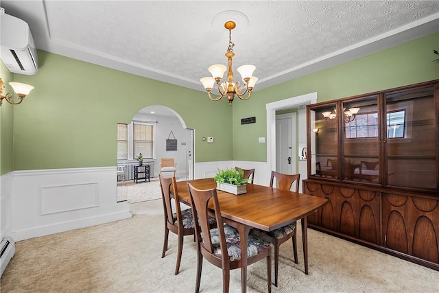 carpeted dining room featuring a wall mounted AC, a chandelier, a textured ceiling, a wainscoted wall, and arched walkways