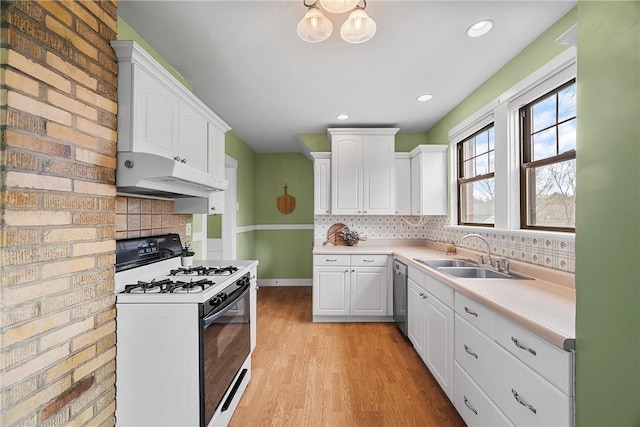 kitchen with stainless steel dishwasher, white cabinets, under cabinet range hood, gas stove, and a sink