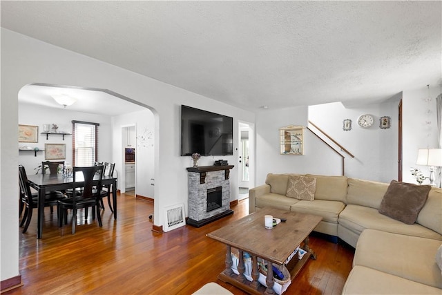 living room featuring visible vents, arched walkways, a fireplace, a textured ceiling, and wood finished floors