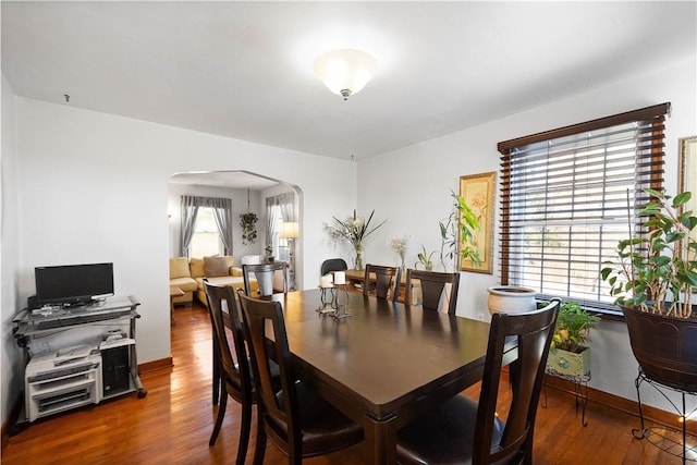 dining room featuring baseboards, arched walkways, and wood finished floors