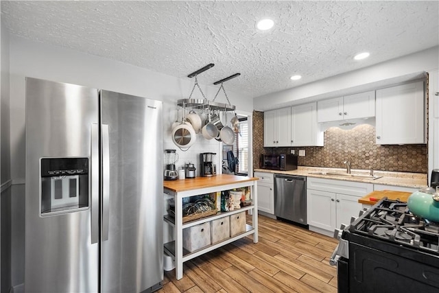 kitchen featuring light wood-type flooring, a textured ceiling, white cabinetry, backsplash, and appliances with stainless steel finishes