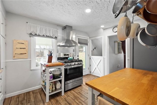 kitchen with a textured ceiling, stainless steel range with gas cooktop, wood finished floors, and wall chimney range hood