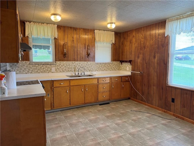 kitchen featuring light countertops, wood walls, white electric range, brown cabinetry, and a sink