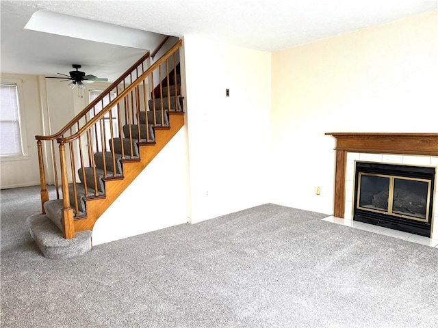 unfurnished living room featuring carpet flooring, a fireplace, a ceiling fan, and stairway