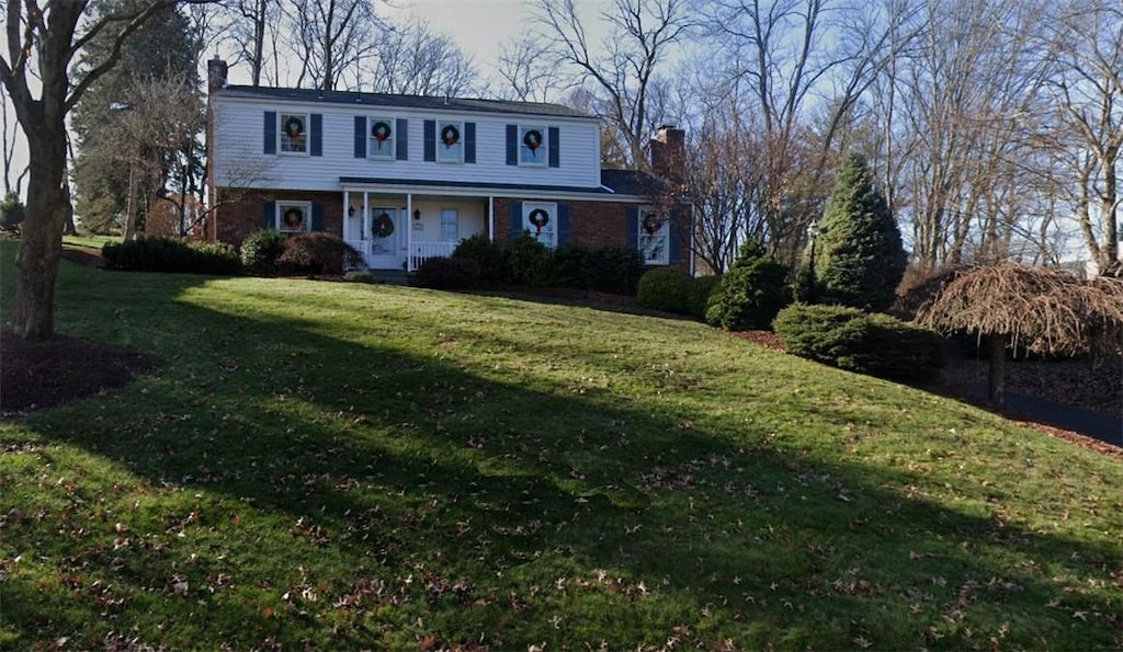 traditional home with a front lawn, a porch, and a chimney