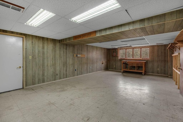 finished below grade area with wooden walls, visible vents, tile patterned floors, and a paneled ceiling