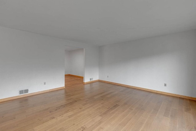 empty room featuring light wood-type flooring, visible vents, and baseboards