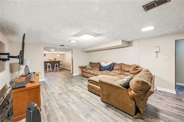 living room featuring visible vents, baseboards, wood finished floors, and a textured ceiling
