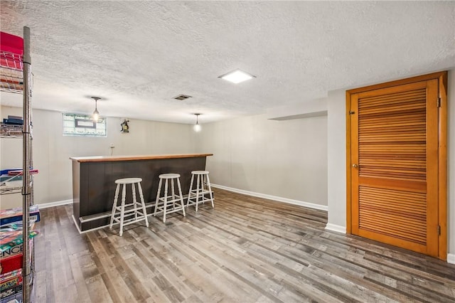 bar with wood finished floors, a textured ceiling, indoor bar, baseboards, and visible vents