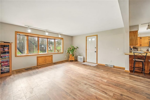 unfurnished living room with light wood finished floors, baseboards, visible vents, and rail lighting