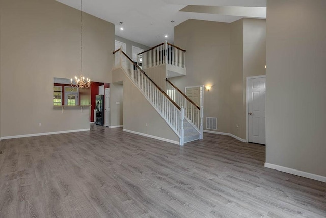unfurnished living room featuring high vaulted ceiling, a chandelier, baseboards, stairway, and wood finished floors