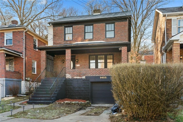 traditional-style home with a chimney, driveway, covered porch, brick siding, and a garage