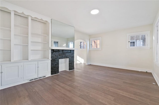 unfurnished living room with dark wood-style floors, visible vents, arched walkways, baseboards, and a fireplace