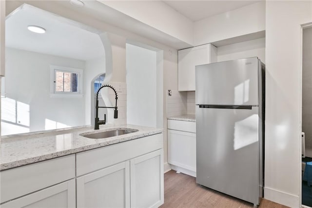 kitchen with white cabinets, light wood-style flooring, a sink, freestanding refrigerator, and light stone counters