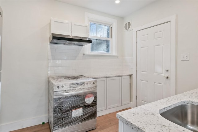 kitchen featuring white cabinets, light wood-type flooring, decorative backsplash, light stone countertops, and under cabinet range hood