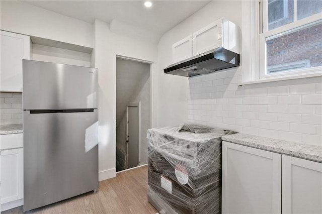 kitchen featuring freestanding refrigerator, extractor fan, tasteful backsplash, and white cabinetry