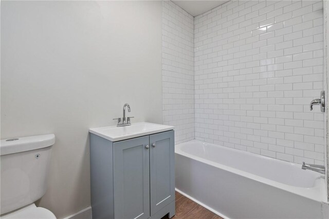 bathroom featuring wood finished floors, toilet, vanity, and bathing tub / shower combination
