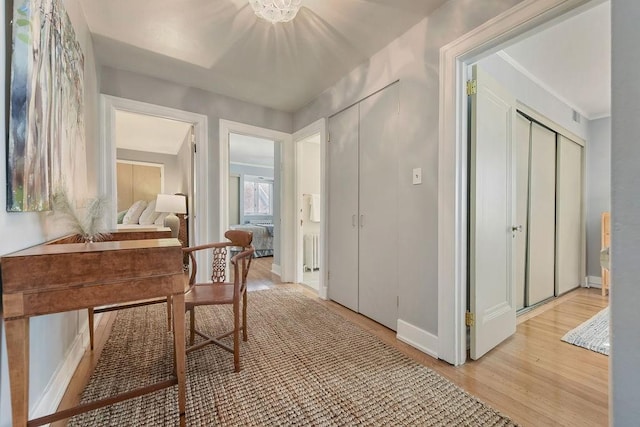 hall featuring radiator heating unit, baseboards, and light wood finished floors