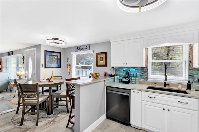 kitchen featuring tasteful backsplash, a sink, dishwasher, light countertops, and white cabinets