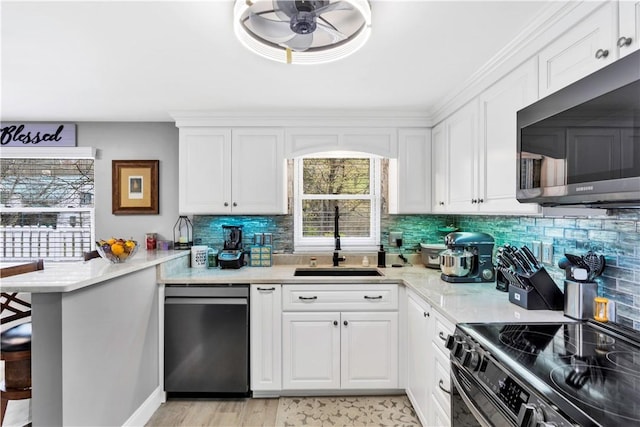 kitchen with white cabinets, stainless steel appliances, a peninsula, a sink, and tasteful backsplash