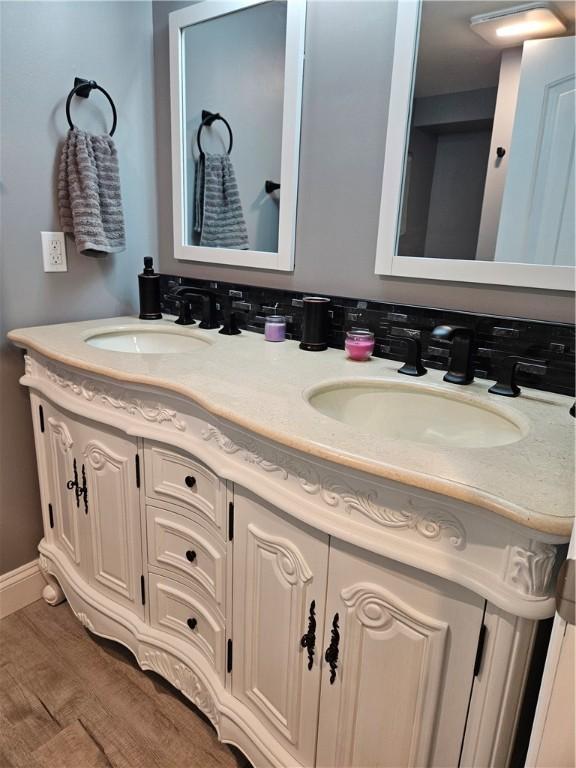 bathroom featuring baseboards, wood finished floors, a sink, and double vanity