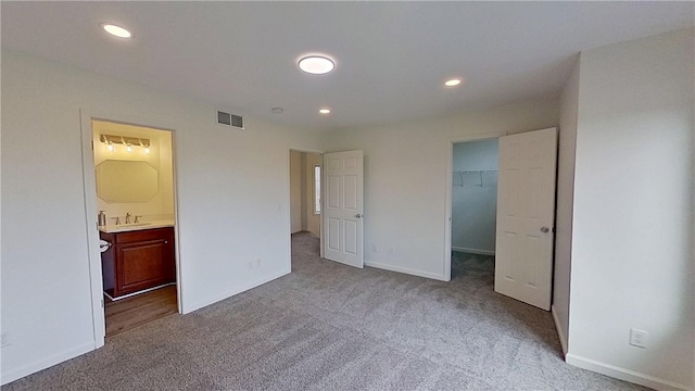 unfurnished bedroom with visible vents, a sink, carpet floors, baseboards, and a spacious closet