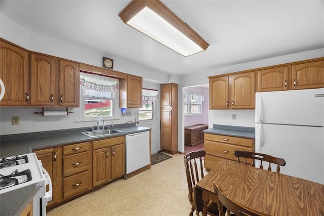 kitchen with brown cabinets, dark countertops, a sink, and white appliances