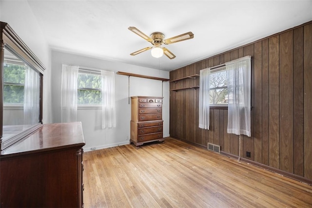 bedroom featuring wooden walls, light wood-type flooring, visible vents, and baseboards