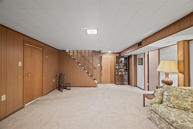 finished basement with stairway, a bar, carpet, wood walls, and visible vents