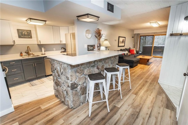 kitchen with stainless steel dishwasher, light wood-style flooring, a sink, and a breakfast bar area