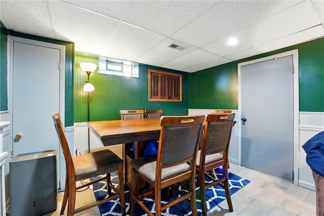 dining area with a decorative wall, a wainscoted wall, a drop ceiling, and visible vents