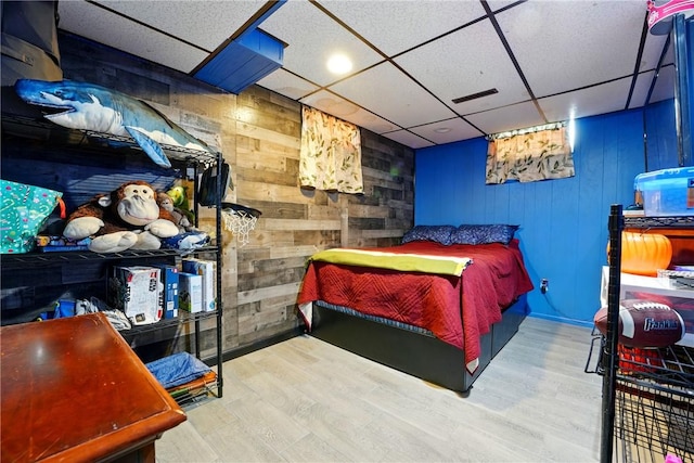 bedroom featuring wooden walls, wood finished floors, and a paneled ceiling