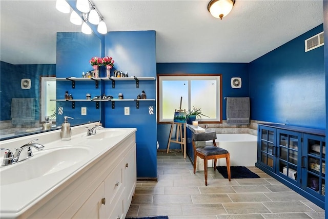 bathroom featuring double vanity, a soaking tub, visible vents, and a sink